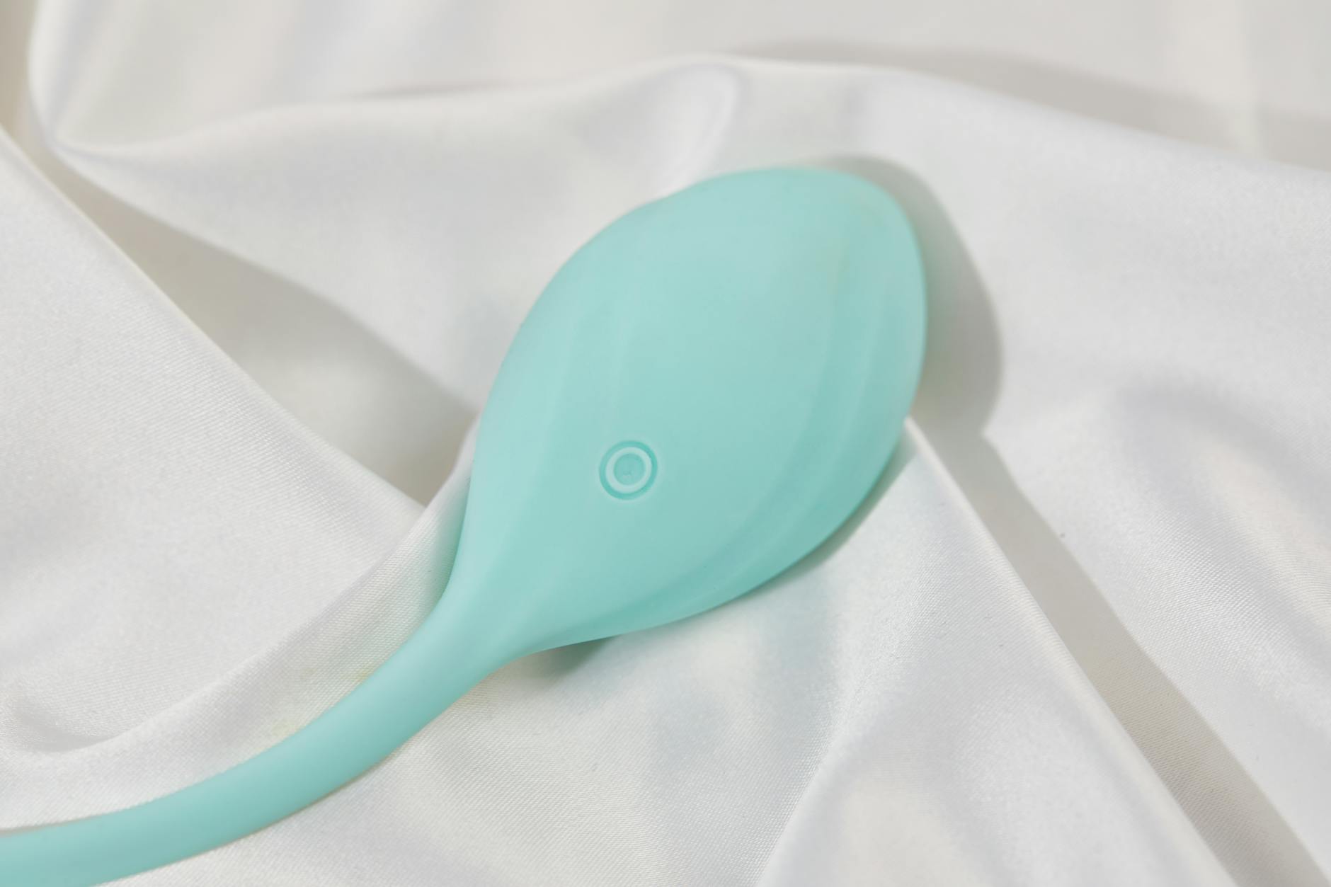 A stylish teal vibrator on smooth white silk fabric, perfect for exploring pleasure without pain.
