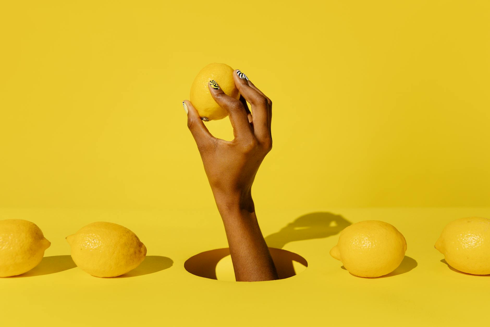 A hand holding a fresh lemon against a bright yellow background, representing renewed sensation and pleasure