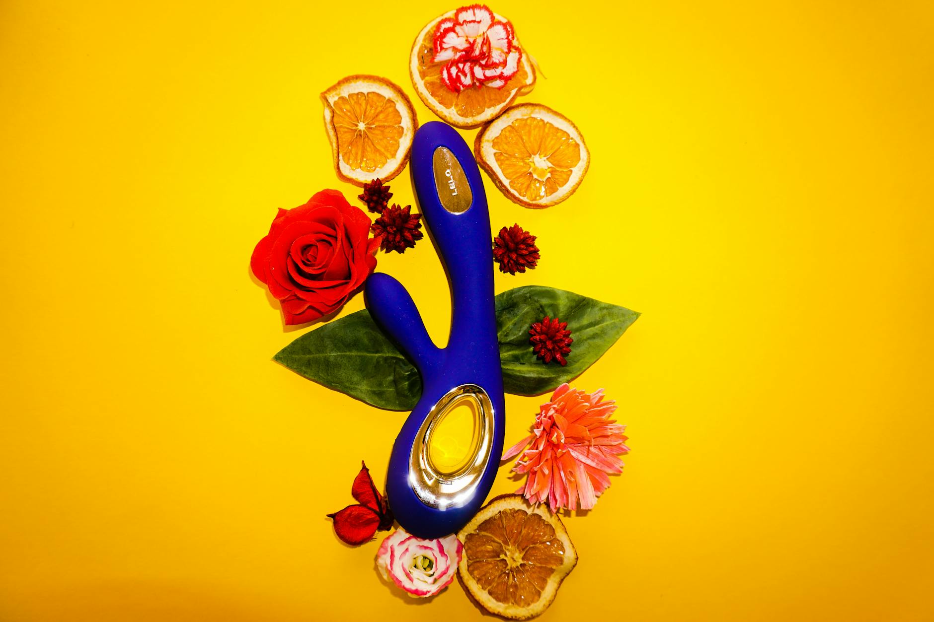 A yellow lemon clitoral vibrator surrounded by fresh lemons and citrus flowers on a bright yellow background