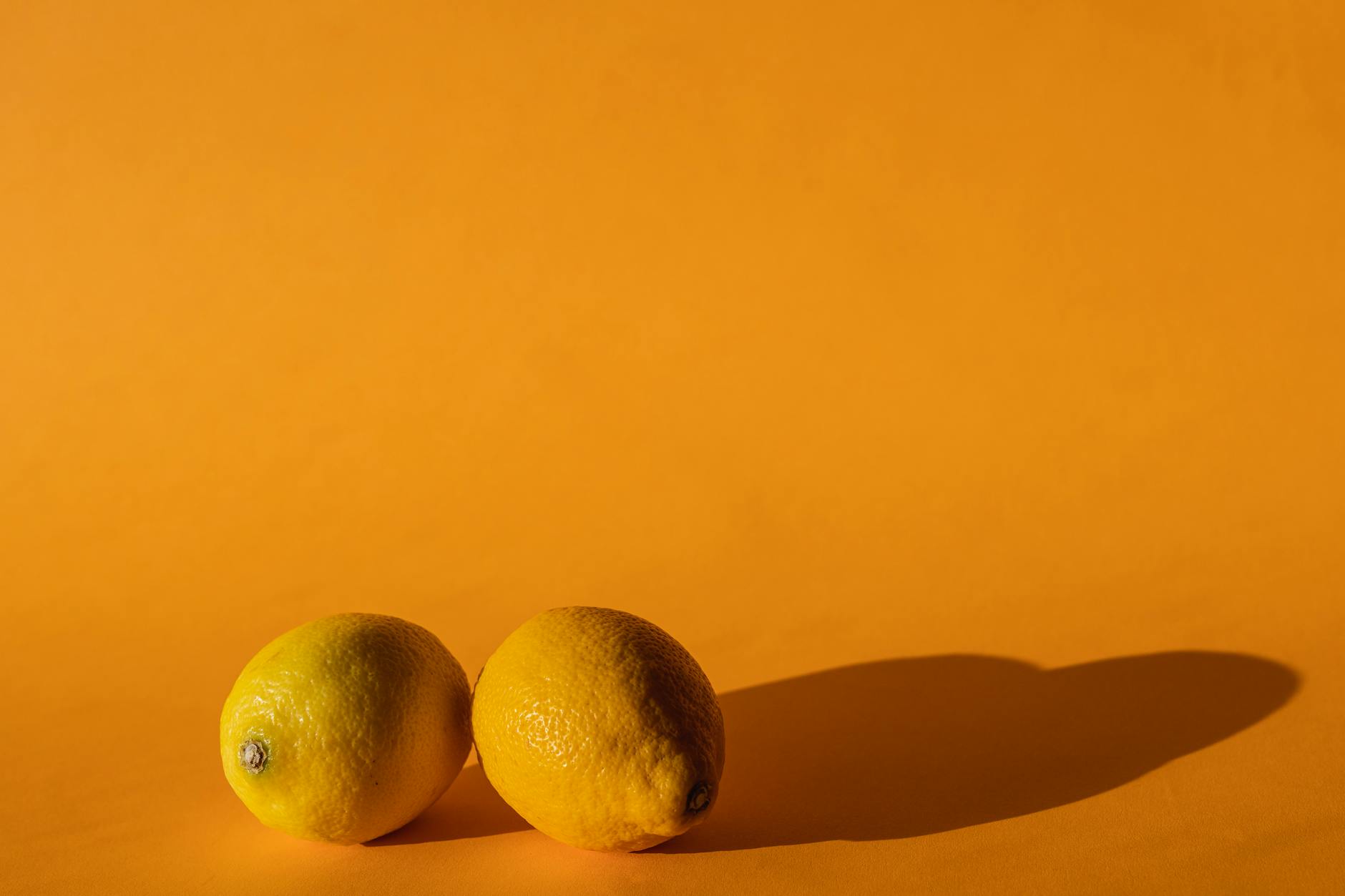 Hand holding an orange clitoral vibrator against a minimalist purple backdrop